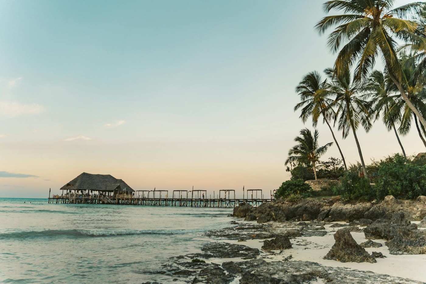 Wybrzeże Zanzibaru o zachodzie słońca: palmy, drewniany pomost, Ocean Indyjski